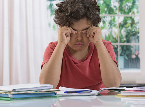 School boy rubbing eyes after long time homework